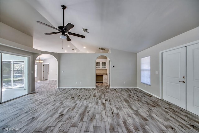 unfurnished living room with arched walkways, vaulted ceiling, wood finished floors, and visible vents