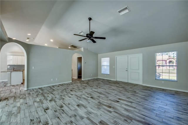 unfurnished living room featuring a wealth of natural light, arched walkways, visible vents, and lofted ceiling