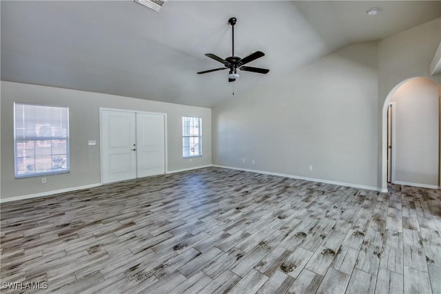 unfurnished living room with a ceiling fan, arched walkways, vaulted ceiling, and wood finished floors