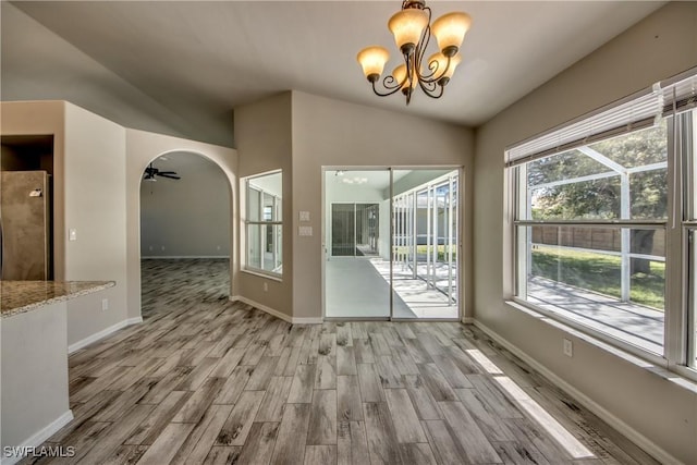 unfurnished dining area featuring arched walkways, ceiling fan with notable chandelier, wood finished floors, baseboards, and vaulted ceiling