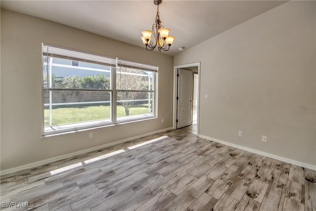 spare room featuring vaulted ceiling, wood finished floors, a chandelier, and baseboards