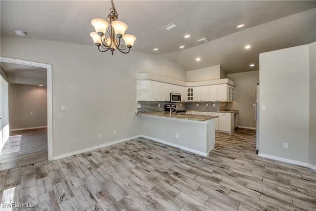 kitchen with light wood-style flooring, a peninsula, white cabinets, stainless steel microwave, and glass insert cabinets