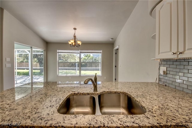 kitchen with decorative backsplash, hanging light fixtures, light stone countertops, an inviting chandelier, and a sink