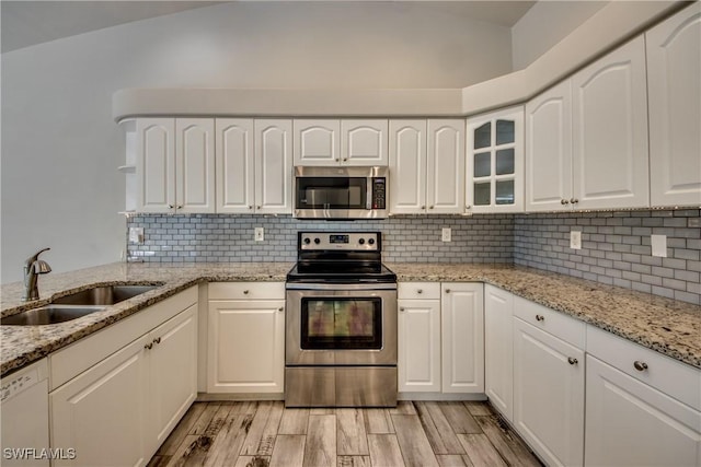 kitchen featuring appliances with stainless steel finishes, a sink, vaulted ceiling, light wood-style floors, and backsplash