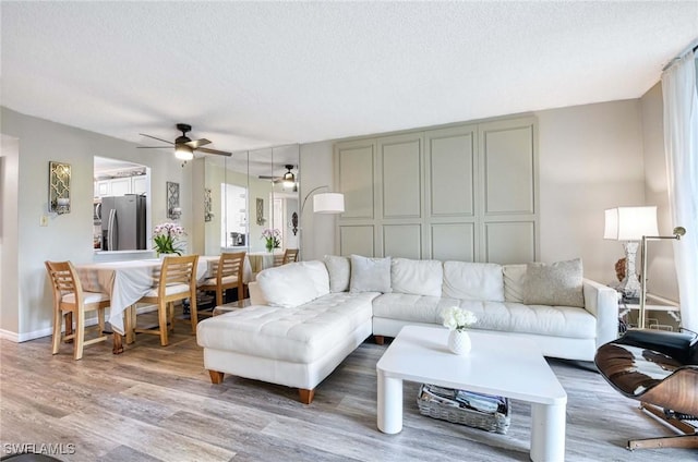 living room with light wood-style floors, ceiling fan, baseboards, and a textured ceiling