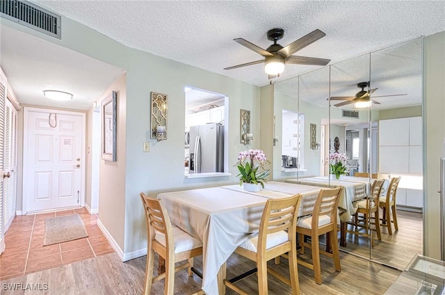 dining area featuring light wood-type flooring, baseboards, visible vents, and a textured ceiling