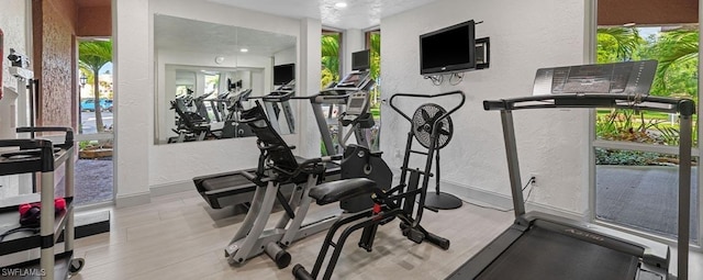 exercise area featuring plenty of natural light, baseboards, wood finished floors, and a textured wall