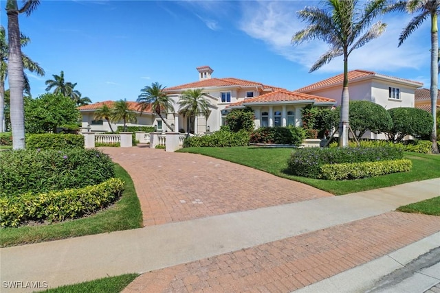 mediterranean / spanish-style home featuring decorative driveway, a tile roof, a front lawn, and stucco siding