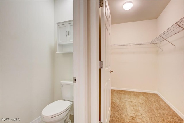 bathroom with toilet, baseboards, and a walk in closet