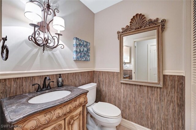 bathroom with a wainscoted wall, wood walls, toilet, and a notable chandelier