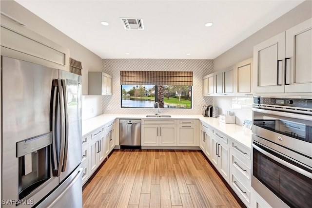 kitchen featuring stainless steel appliances, a sink, visible vents, light wood-type flooring, and backsplash