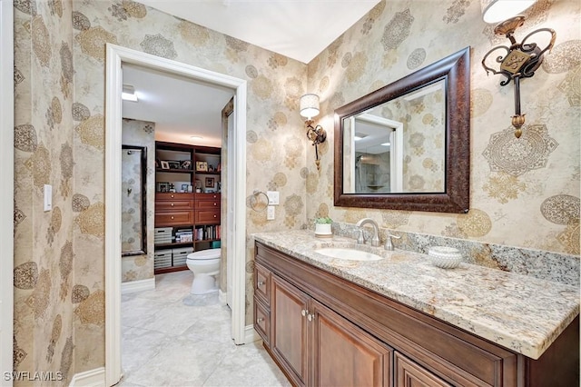 bathroom with baseboards, vanity, toilet, and wallpapered walls