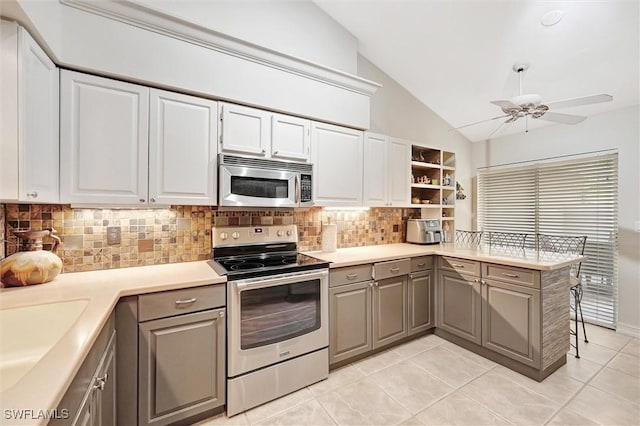 kitchen featuring stainless steel appliances, gray cabinetry, lofted ceiling, tasteful backsplash, and a peninsula