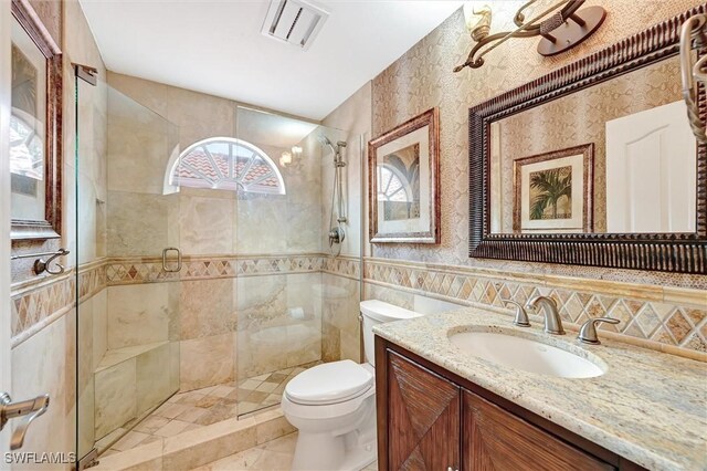 bathroom with toilet, a stall shower, vanity, tile walls, and tile patterned floors