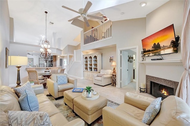 tiled living area featuring high vaulted ceiling, ceiling fan with notable chandelier, visible vents, a lit fireplace, and stairway