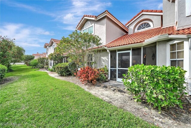 back of property featuring a tiled roof, stucco siding, a yard, and a sunroom