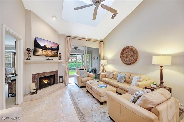 living area with a ceiling fan, light tile patterned floors, high vaulted ceiling, a tile fireplace, and a skylight