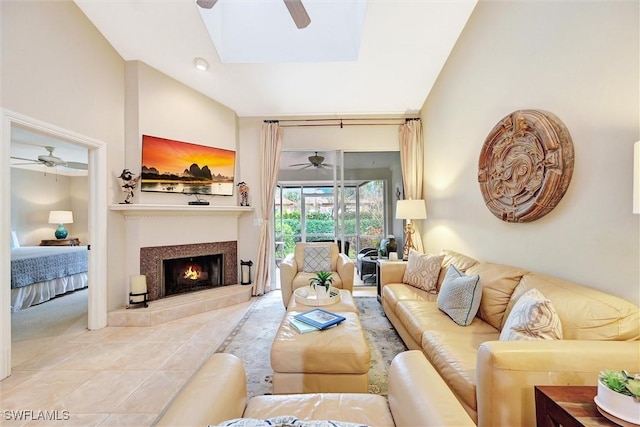 living area with a ceiling fan, vaulted ceiling, a tile fireplace, a skylight, and tile patterned flooring