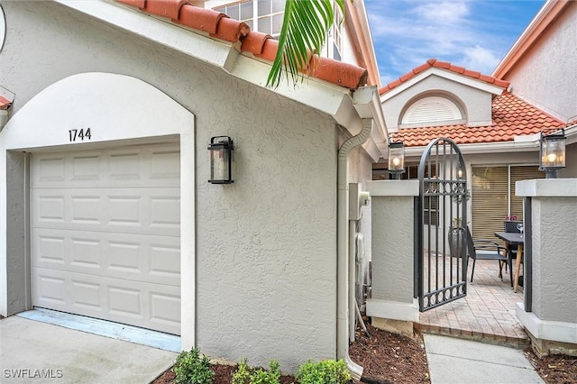 view of exterior entry featuring stucco siding, a gate, a tile roof, and a garage