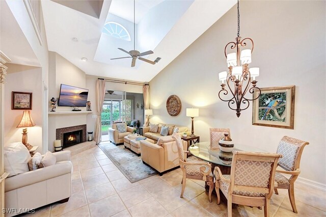 living area with high vaulted ceiling, a ceiling fan, light tile patterned floors, a chandelier, and a warm lit fireplace