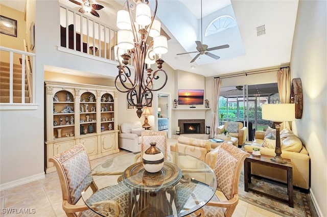 dining space featuring high vaulted ceiling, ceiling fan, a lit fireplace, a chandelier, and baseboards