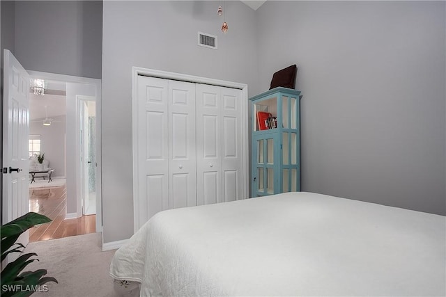 bedroom featuring wood finished floors, visible vents, baseboards, a closet, and a towering ceiling