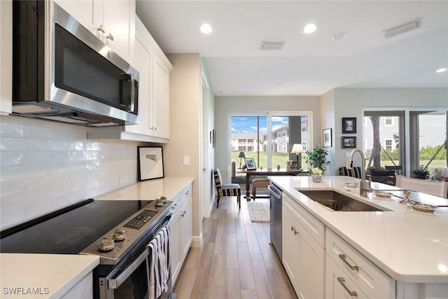 kitchen featuring light wood finished floors, visible vents, tasteful backsplash, appliances with stainless steel finishes, and a sink