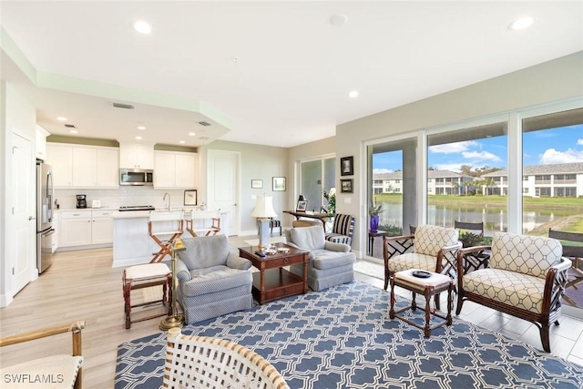 living area featuring recessed lighting, a water view, and light wood-style floors