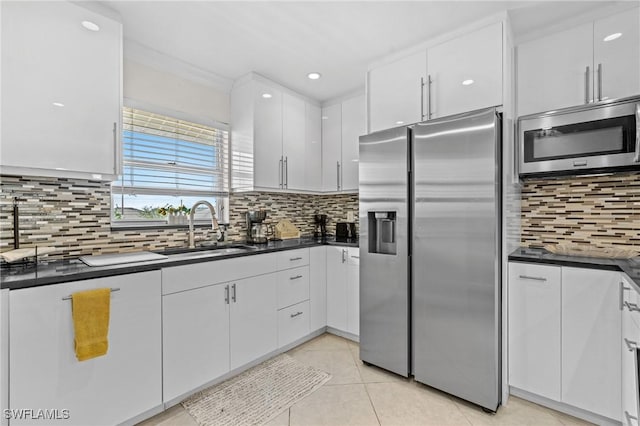 kitchen with light tile patterned flooring, a sink, appliances with stainless steel finishes, white cabinetry, and dark countertops