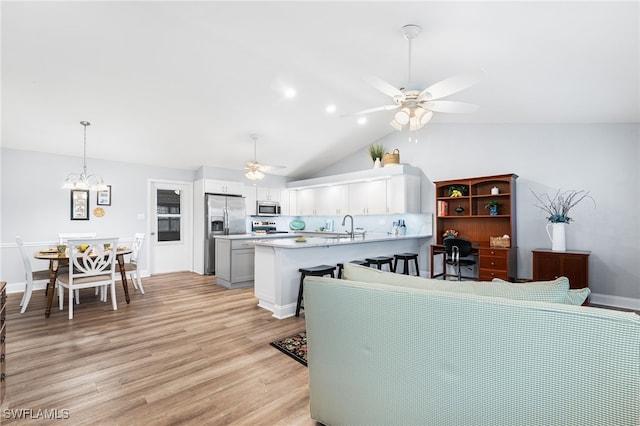 kitchen featuring light wood-style flooring, ceiling fan with notable chandelier, stainless steel appliances, a peninsula, and light countertops