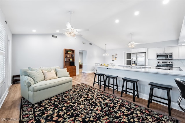 living area featuring lofted ceiling, ceiling fan with notable chandelier, light wood-type flooring, and visible vents