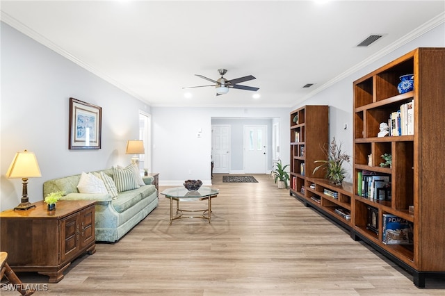 living room featuring light wood-type flooring, visible vents, a ceiling fan, and ornamental molding