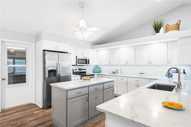 kitchen featuring light stone counters, gray cabinetry, stainless steel appliances, a sink, and vaulted ceiling