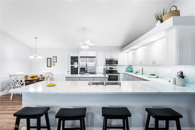 kitchen with decorative backsplash, appliances with stainless steel finishes, a sink, light stone countertops, and a peninsula