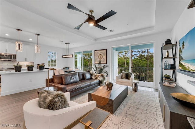 living room with visible vents, a raised ceiling, ceiling fan, light wood-type flooring, and recessed lighting