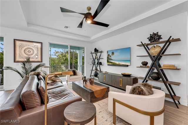 living room with light wood-style floors, a raised ceiling, visible vents, and a ceiling fan