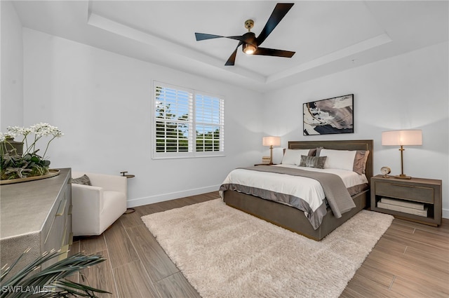 bedroom featuring a tray ceiling, ceiling fan, baseboards, and wood finished floors