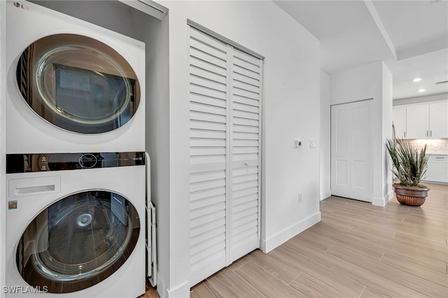 clothes washing area featuring stacked washer and clothes dryer, light wood finished floors, recessed lighting, laundry area, and baseboards