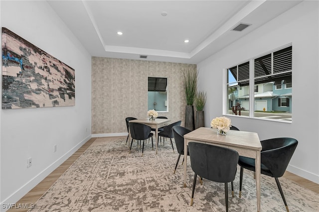 dining area with a tray ceiling, wood finished floors, visible vents, and baseboards