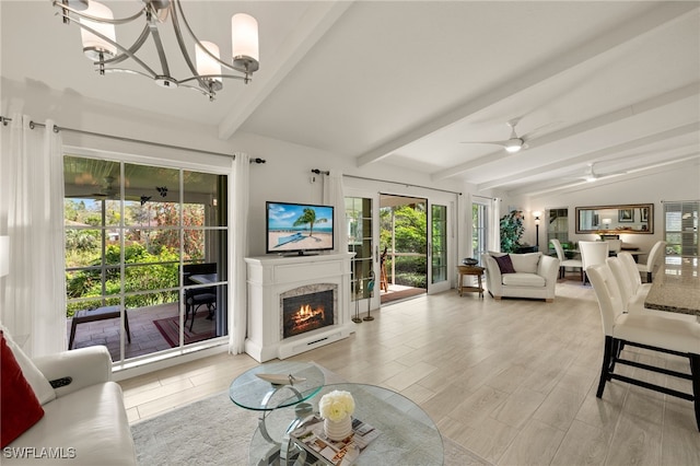 living room featuring light wood finished floors, ceiling fan with notable chandelier, a warm lit fireplace, and vaulted ceiling with beams