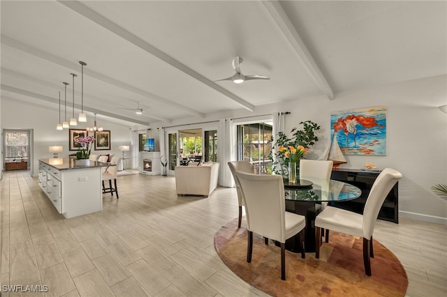 dining space featuring wood finish floors, ceiling fan with notable chandelier, a warm lit fireplace, baseboards, and vaulted ceiling with beams