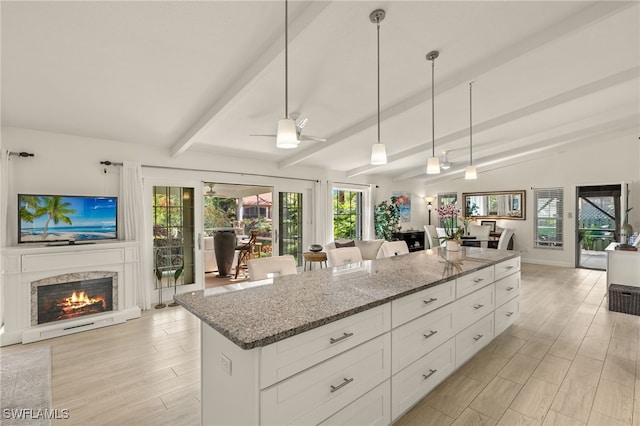 kitchen featuring dark stone countertops, vaulted ceiling with beams, a fireplace, and open floor plan