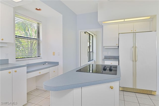 kitchen with built in desk, black electric stovetop, light tile patterned floors, freestanding refrigerator, and white cabinetry