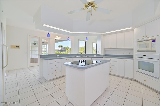 kitchen with white appliances, light tile patterned floors, a peninsula, white cabinetry, and a sink