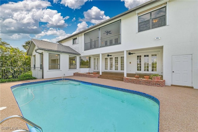 rear view of property with french doors, stucco siding, ceiling fan, a balcony, and an outdoor pool