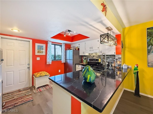 kitchen featuring a tray ceiling, stainless steel appliances, dark countertops, tasteful backsplash, and a peninsula