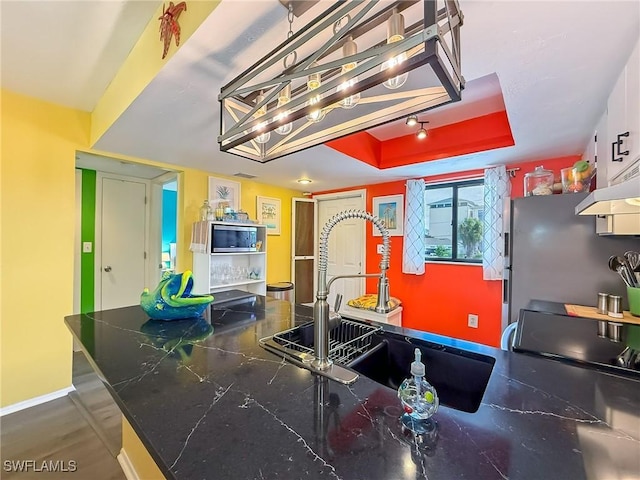 kitchen with baseboards, a raised ceiling, dark countertops, appliances with stainless steel finishes, and a sink