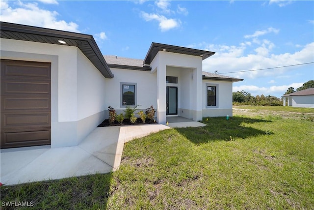 view of exterior entry featuring an attached garage, a lawn, and stucco siding