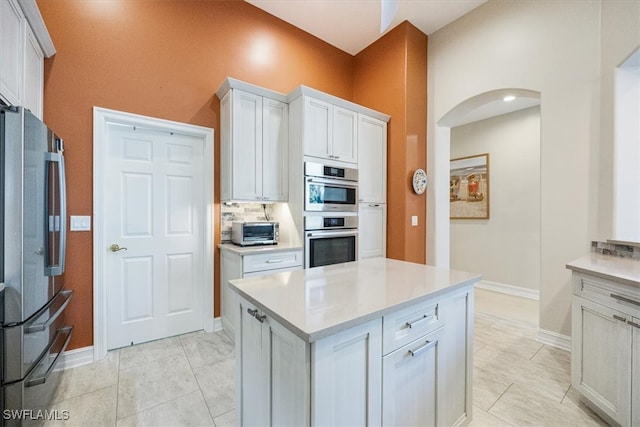 kitchen with tasteful backsplash, a toaster, light countertops, appliances with stainless steel finishes, and arched walkways