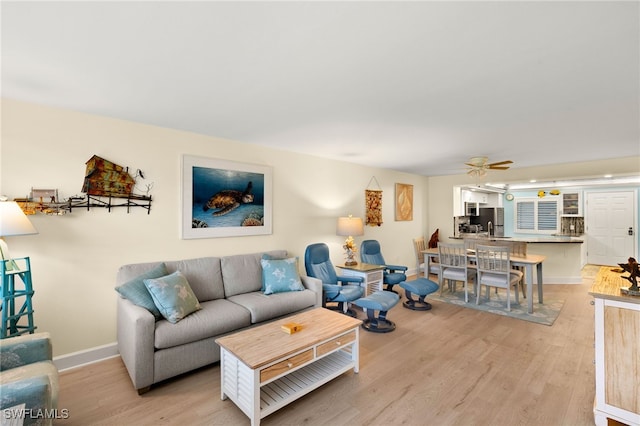 living area with light wood-type flooring, ceiling fan, and baseboards